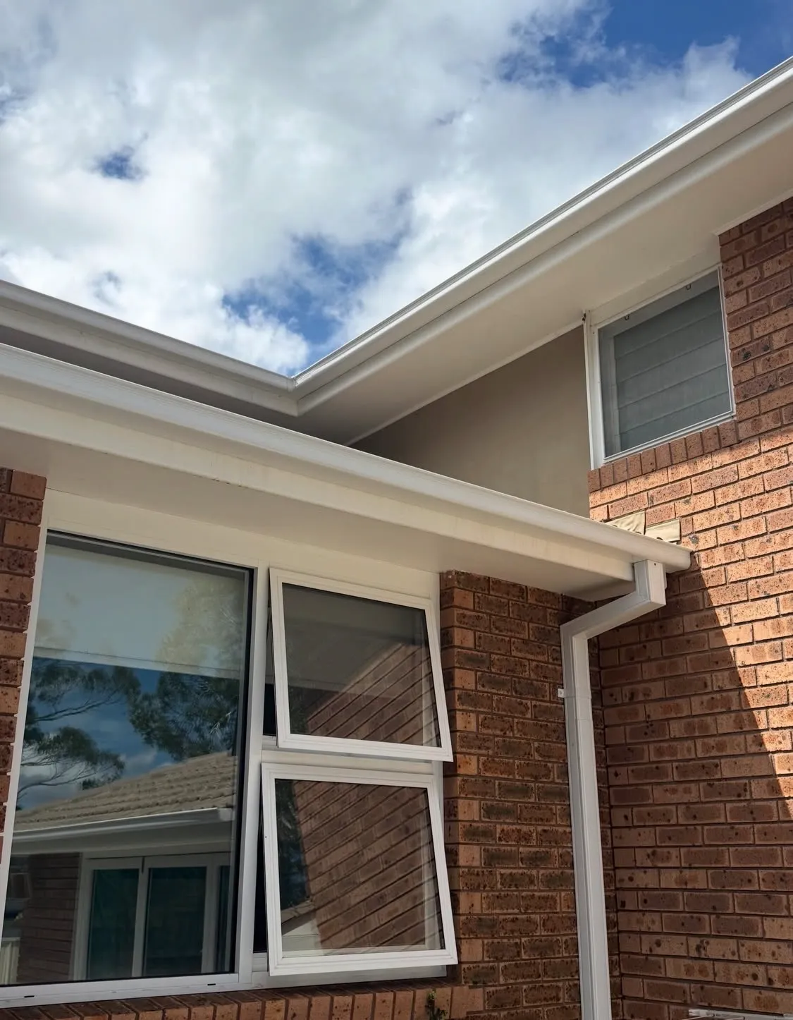 Cream guttering and a matching downpipe along a two-storey brick home on the Central Coast